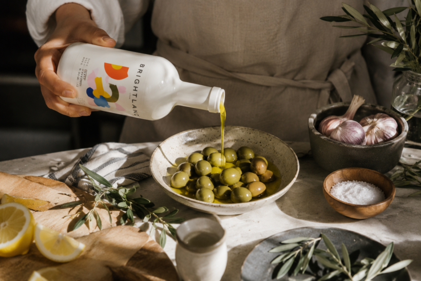 Brightland olive oil being poured over olives with garlic, lemon and fresh ingredients in a warm kitchen